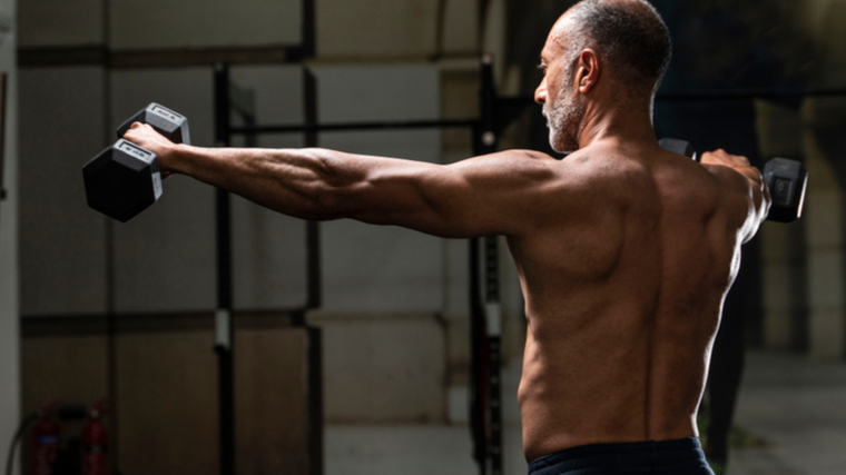 shirtless person in gym performing dumbbell shoulder exercise